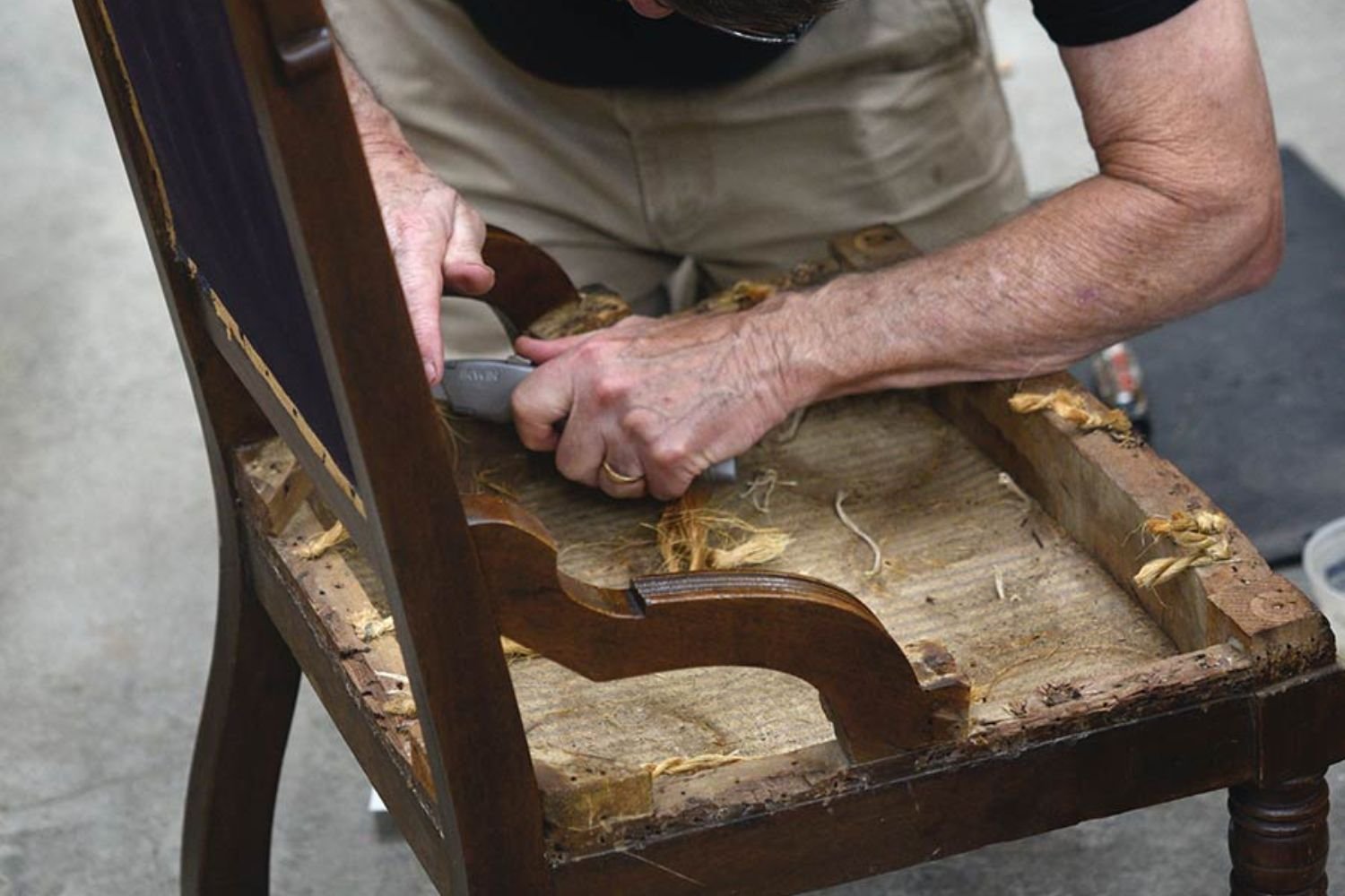 A man repairs an old wooden chair, focused on restoring its structure and appearance in a well-lit workshop.