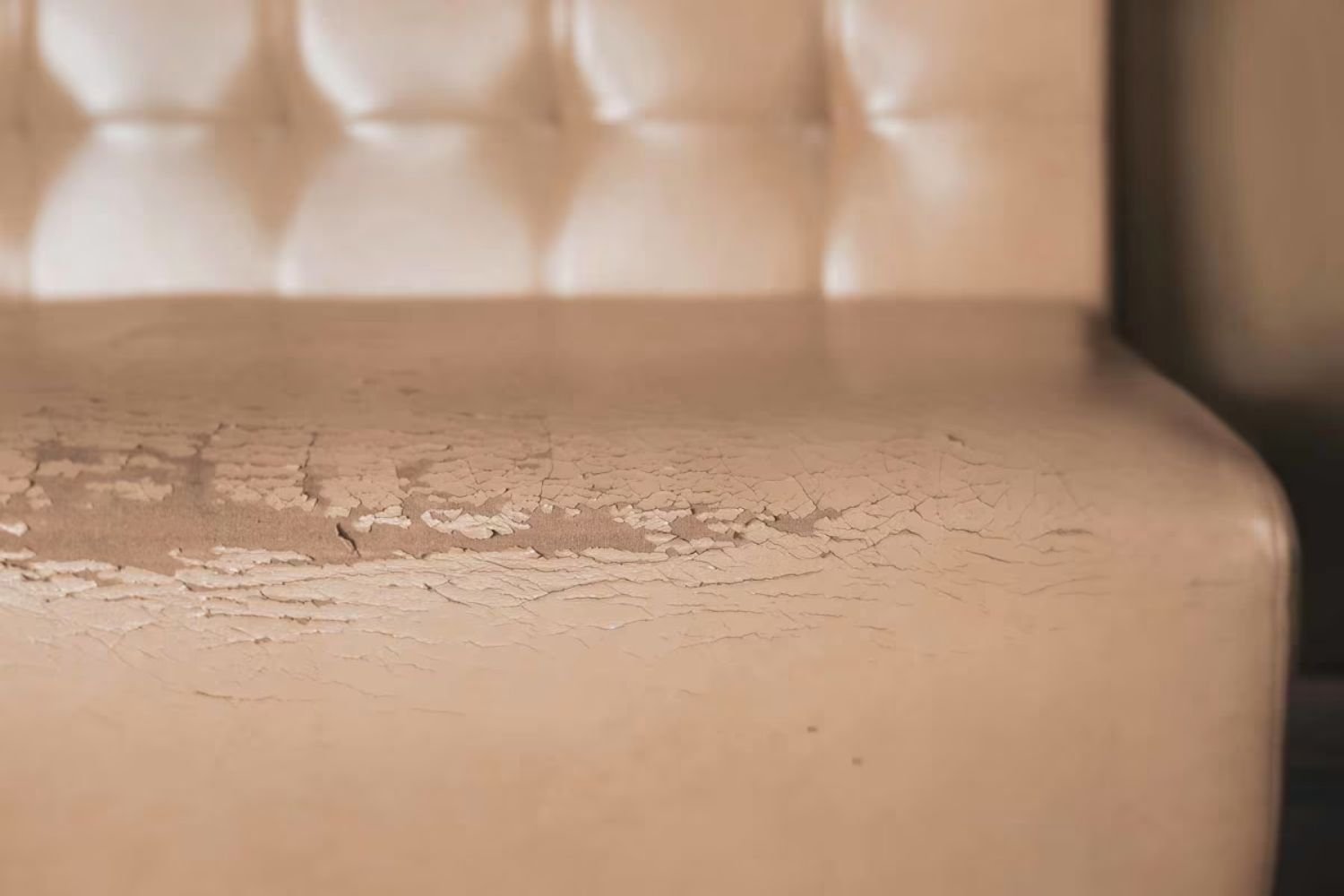 Close-up of a worn tan leather couch with cracks and fading, set against a brown wall.