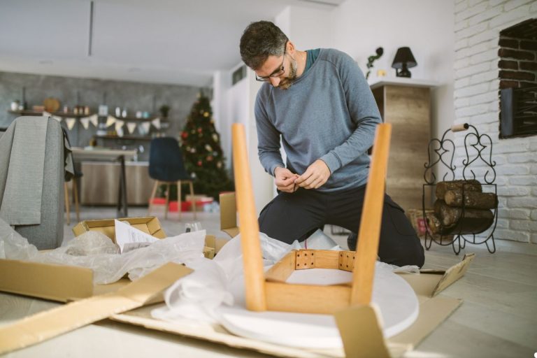 A man is assembling a chair in his living room, surrounded by tools and furniture.