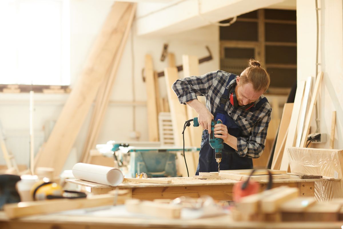 A man using a drill on a wooden table, focused on his task in a well-lit workspace. 