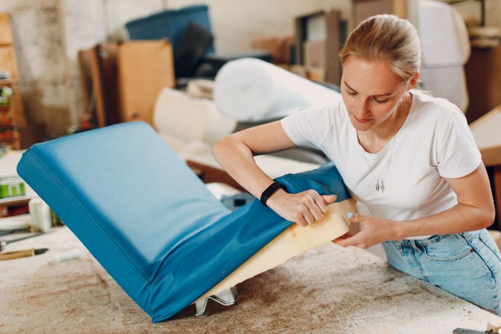 A woman sits on a chair with a blue cover, focused on her work, surrounded by a bright and organized workspace.