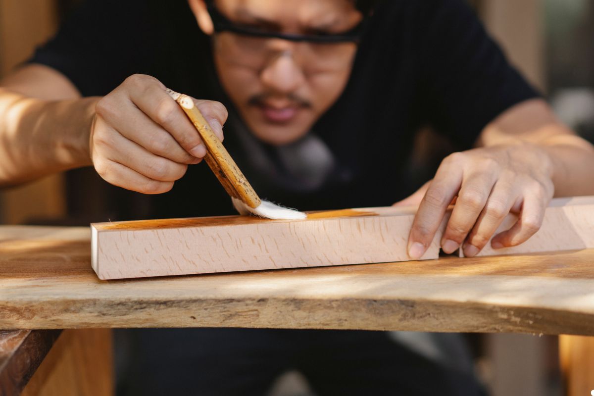 A man shapes a piece of wood using a wooden block as a tool in a workshop setting.