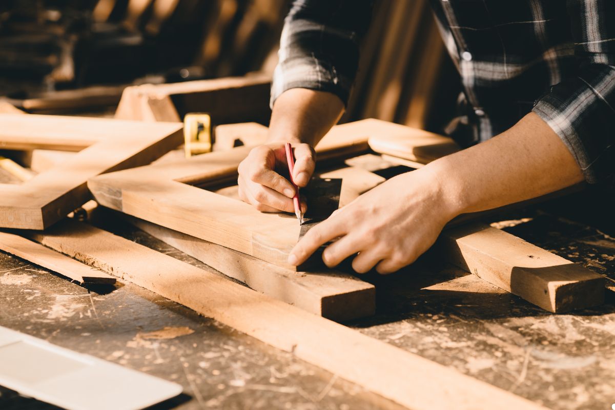 A man carefully sanding a wooden piece of furniture in a workshop, focused on his craftsmanship.