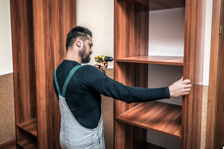 A man focused on assembling a wooden cabinet in a workshop, surrounded by tools and wood pieces.